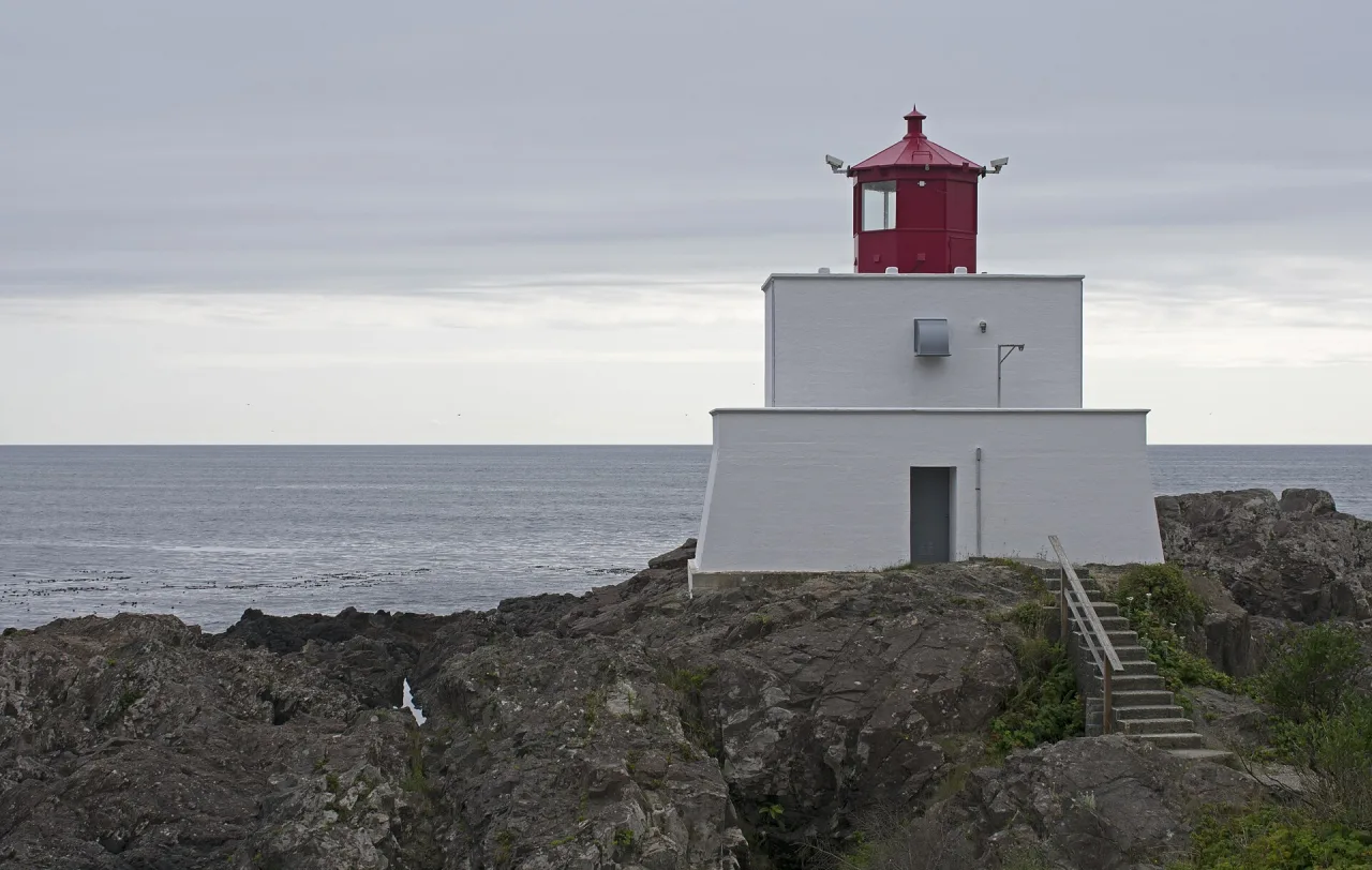 The white and red Amphitrite Point Lighthouse on the rocky shore of Ucluelet