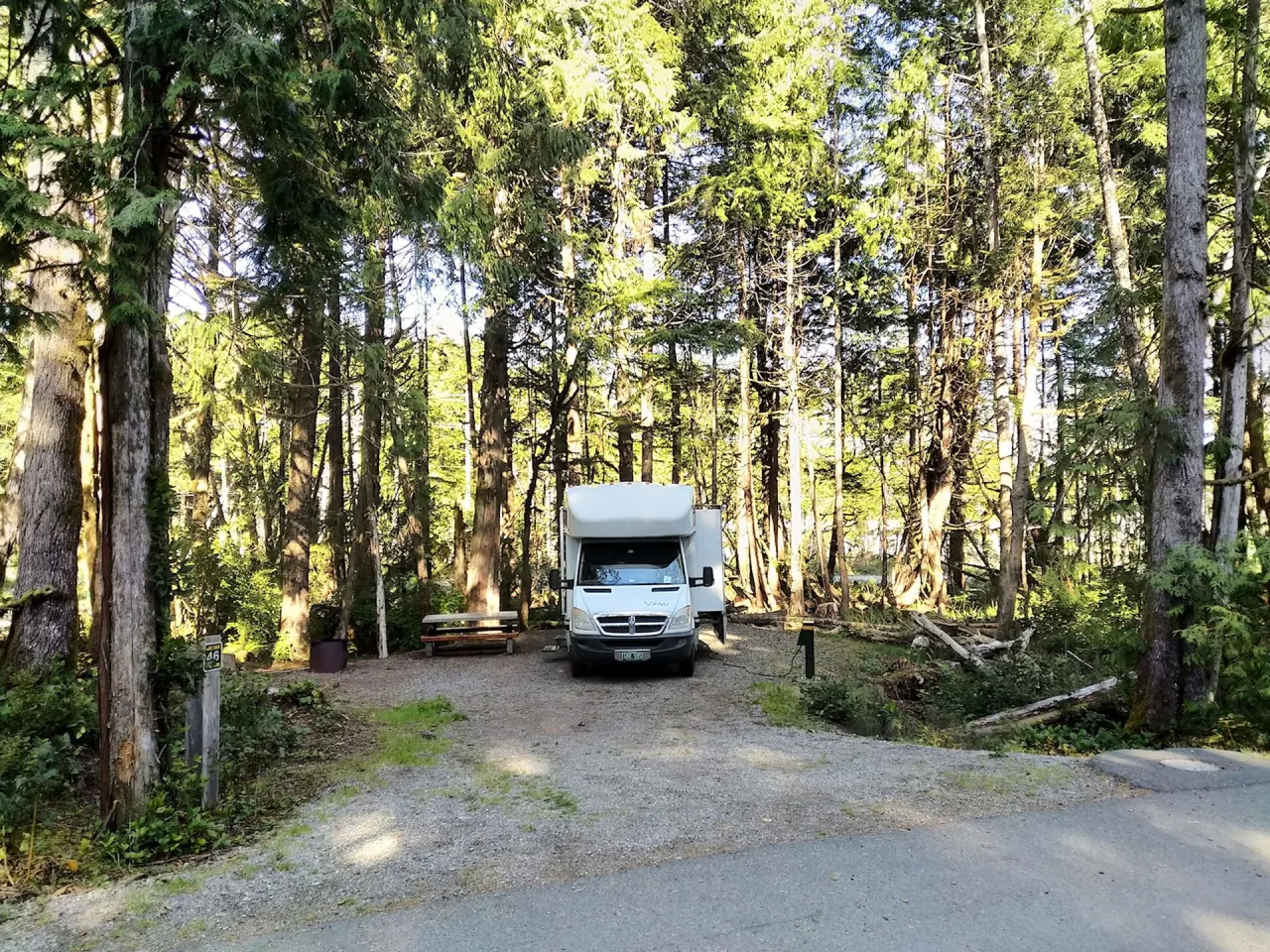 A camper van parked at a forested campsite at Green Point Campground, Pacific Rim National Park Reserve