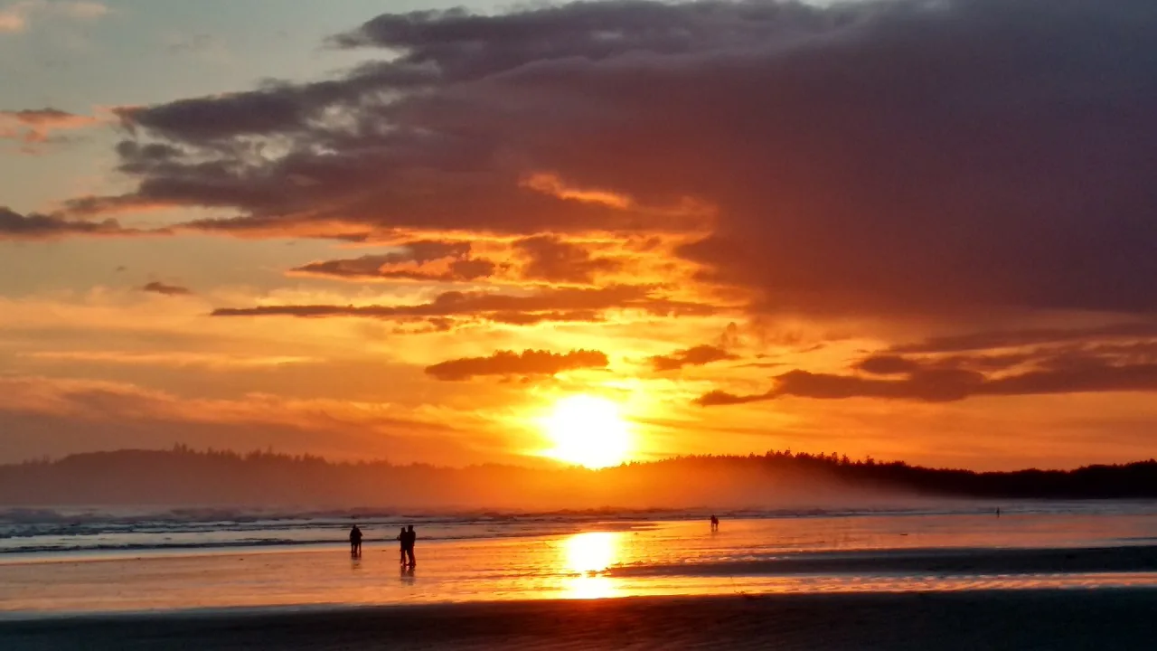 People silhouetted on Long Beach under an orange sunset sky