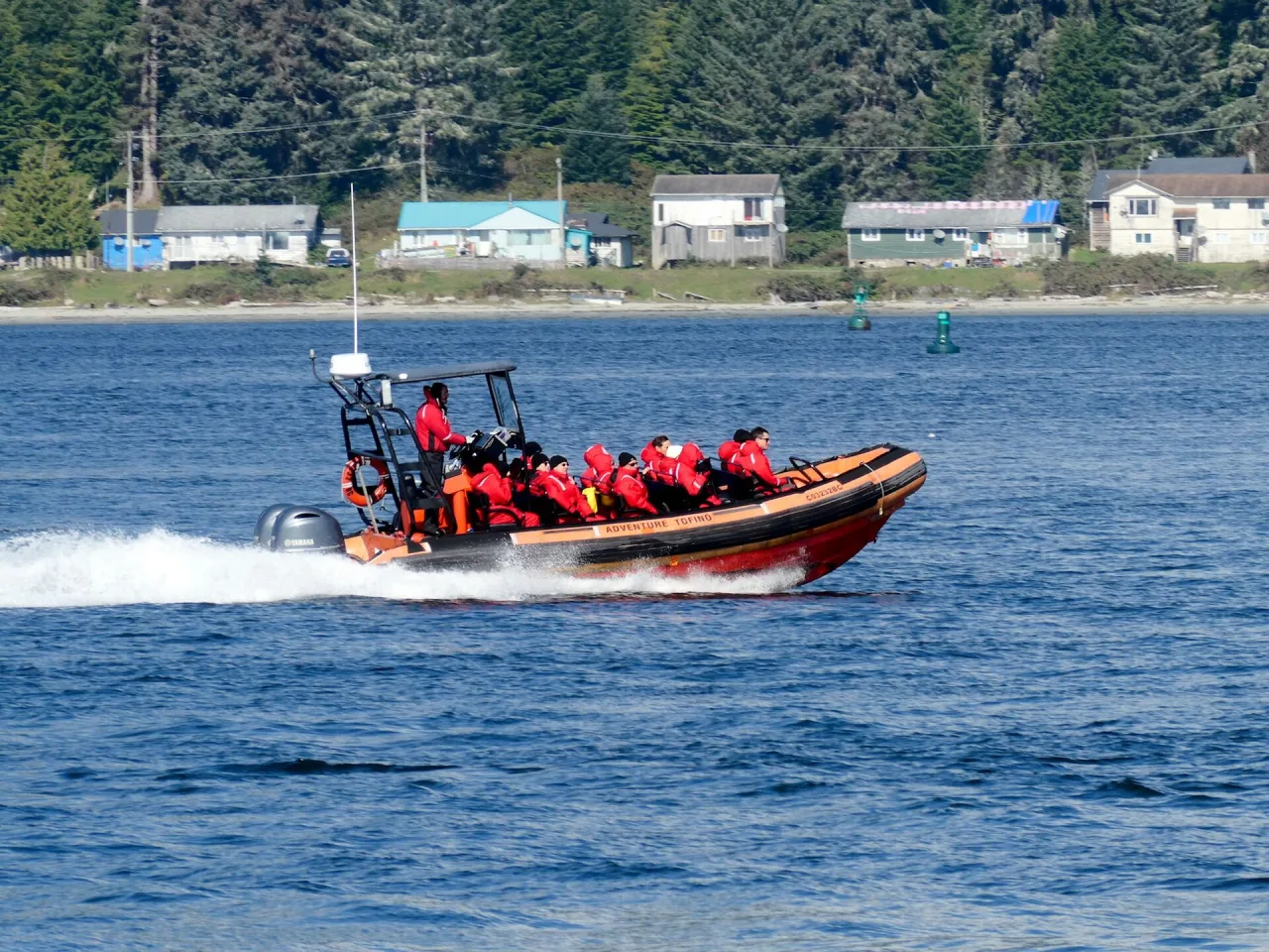 A red tour boat speeding past Opitsaht across the harbour from Tofino